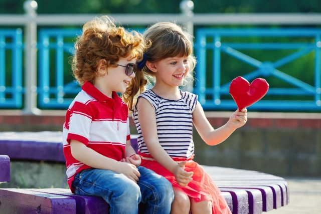 Kisfiú és kislány egy szivecskét bámul mosolyogva.