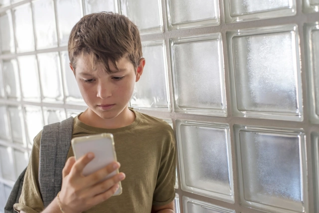 Kiskamasz aggódva figyeli a telefonját egy üvegfal előtt